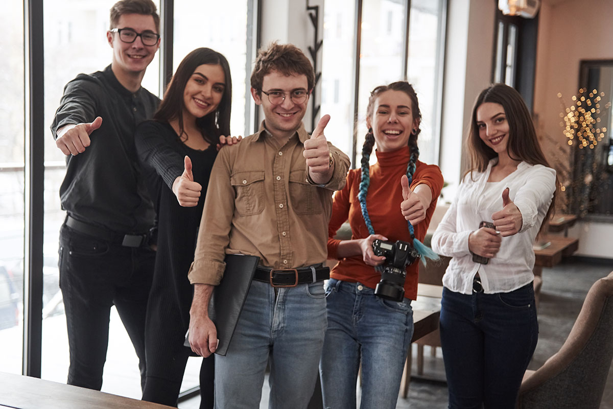 Five young people shows thumbs up gesture and looking straight into the camera.